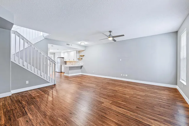 a view of an empty room with wooden floor and a kitchen