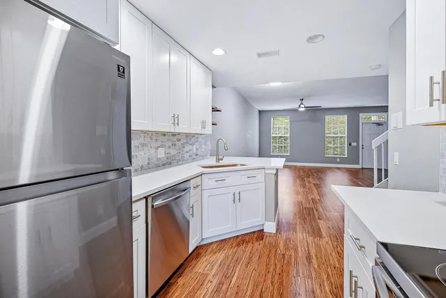 a kitchen with a sink a refrigerator a stove and white cabinets with wooden floor