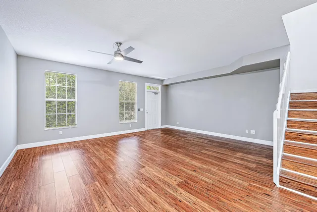an empty room with wooden floor ceiling fan and windows