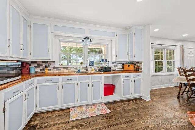 a open kitchen with granite countertop a stove a sink and white cabinets with wooden floor