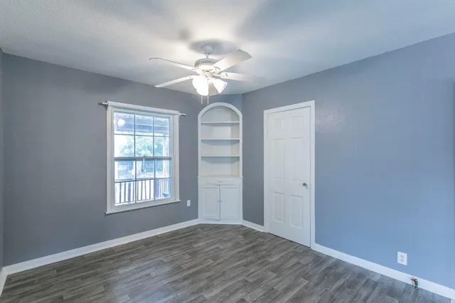 an empty room with wooden floor chandelier fan and windows