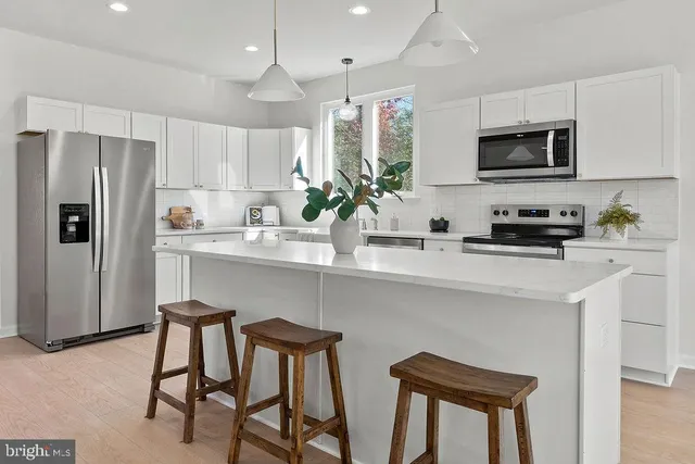 a kitchen with stainless steel appliances a sink a stove a refrigerator cabinets and a dining table