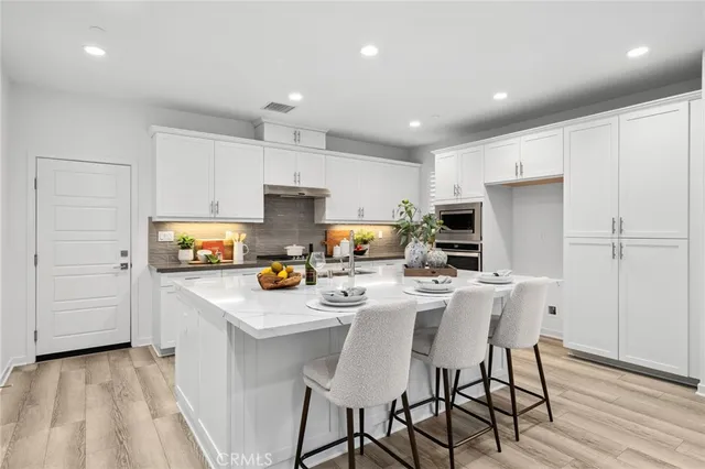 a kitchen with stainless steel appliances a stove a sink a refrigerator white cabinets and wooden floor