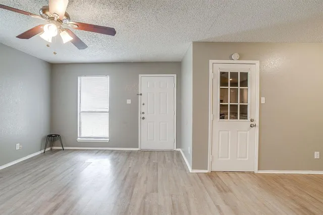 an empty room with wooden floor chandelier fan and windows