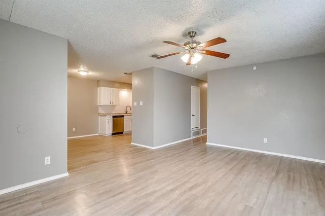 a view of an empty room and kitchen with wooden floor