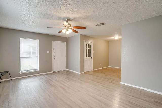 an empty room with wooden floor chandelier fan and windows