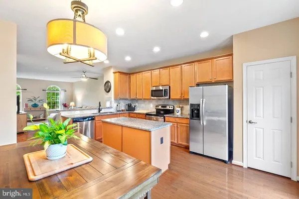 a kitchen with stainless steel appliances granite countertop a refrigerator a stove a sink a dining table and chairs with wooden floor