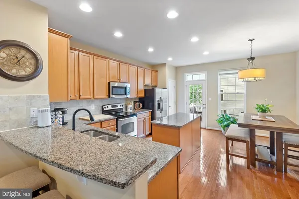 a kitchen with stainless steel appliances granite countertop a stove top oven a sink a dining table and chairs with wooden floor