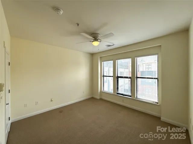 an empty room with chandelier fan and windows