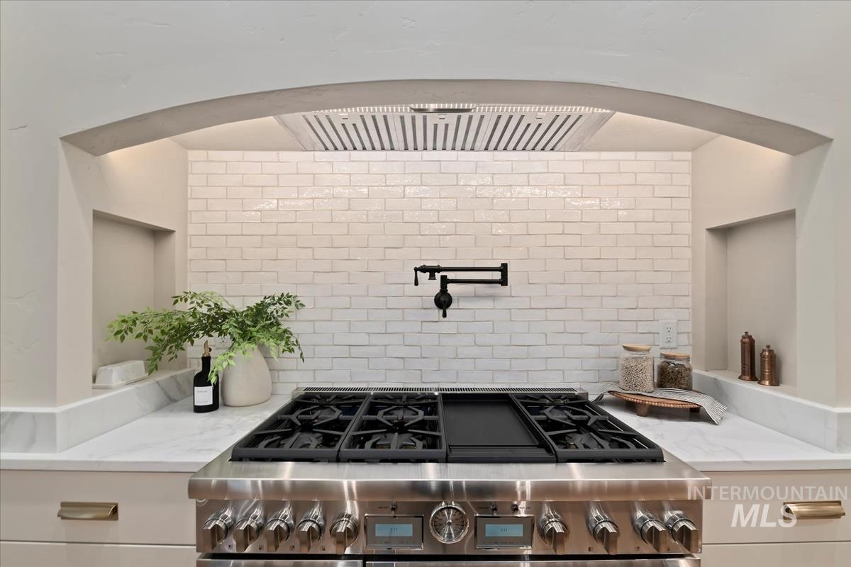 196 North Timber Wolf Place Eagle, ID 83616 - Photo 6 of 50 Kitchen with light stone countertops, range hood, stainless steel gas cooktop, and tasteful backsplash