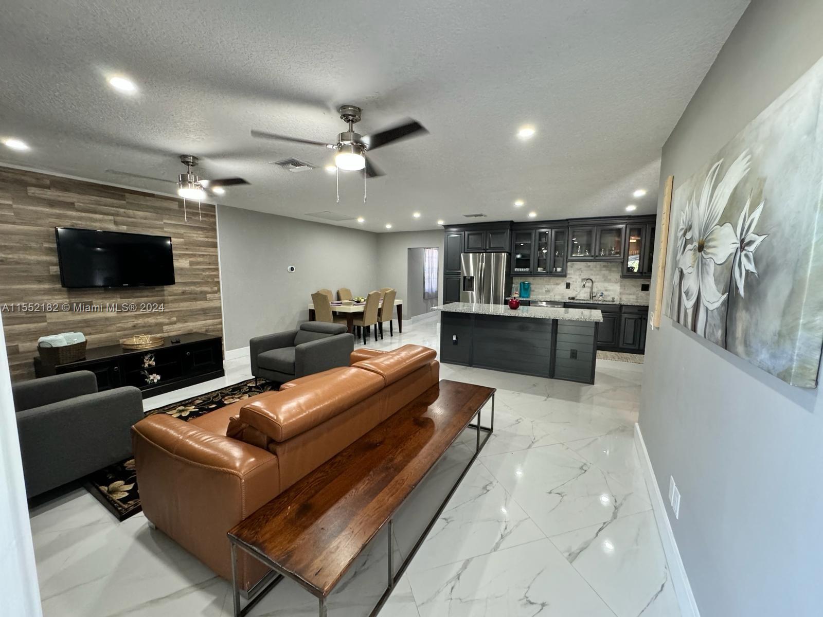 a large living room with stainless steel appliances furniture a flat screen tv and a kitchen view