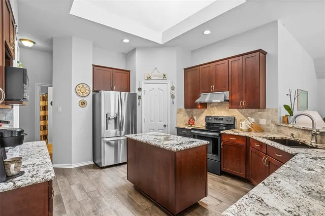 a kitchen with stainless steel appliances granite countertop a stove a sink dishwasher and a refrigerator with wooden floor