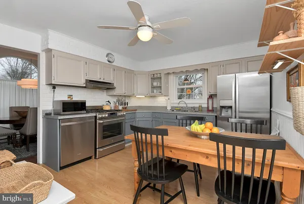 a kitchen with stainless steel appliances granite countertop a stove top oven a refrigerator a sink and a dining table with white cabinets