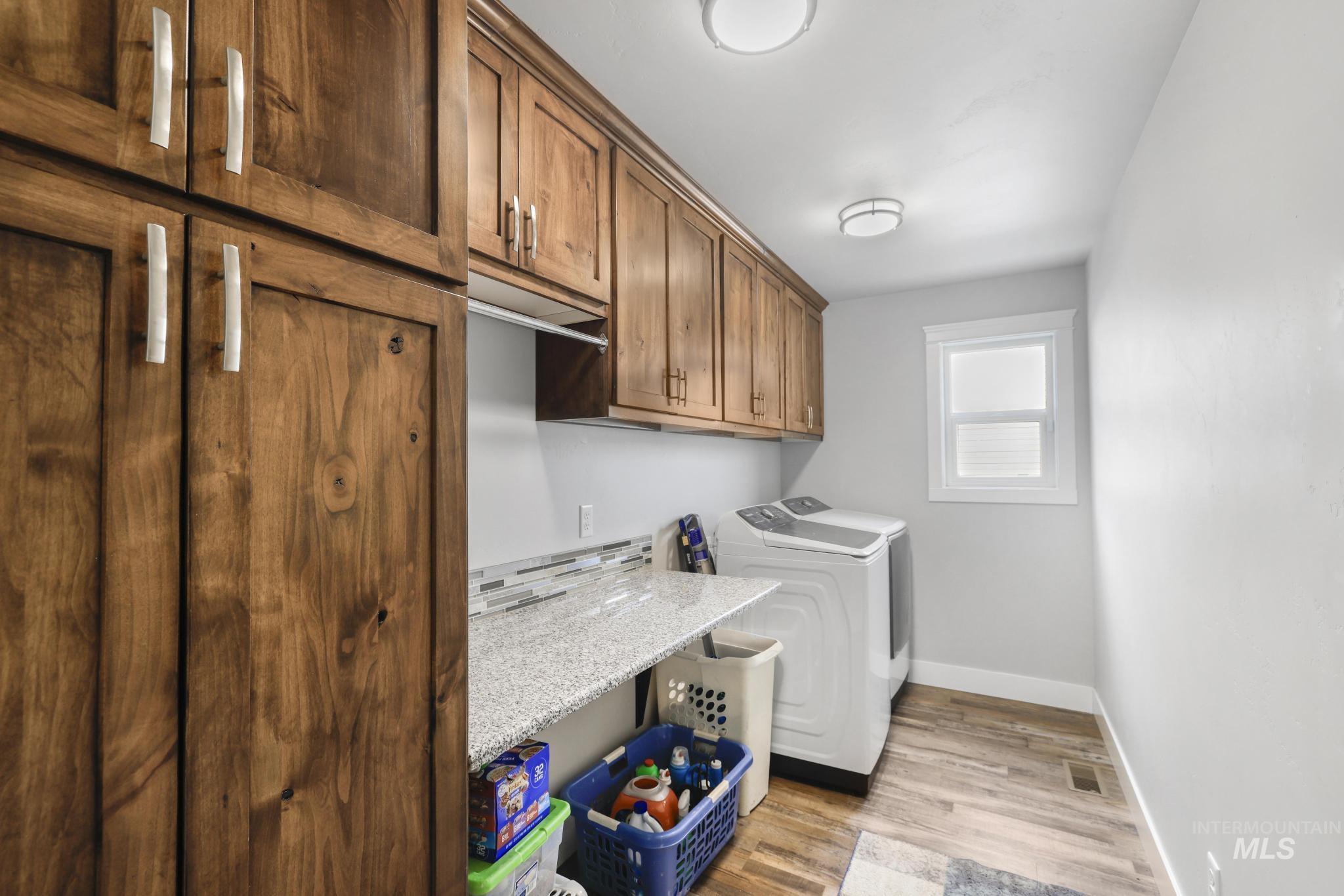 1150 Kimberly Meadows Road Kimberly, ID 83341 - Photo 13 of 32 Laundry room featuring rich wood cabinetry with ample storage, a light-toned countertop, a contemporary mosaic tile backsplash, and wood-finish flooring