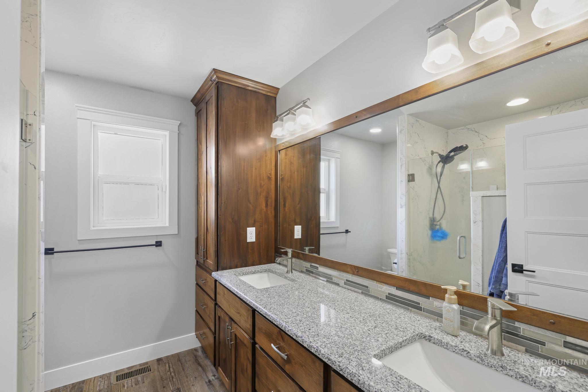 1150 Kimberly Meadows Road Kimberly, ID 83341 - Photo 17 of 32 Bathroom featuring a double vanity with granite countertops, wood-finish cabinetry, an oversized mirror, and a walk-in shower with a glass enclosure