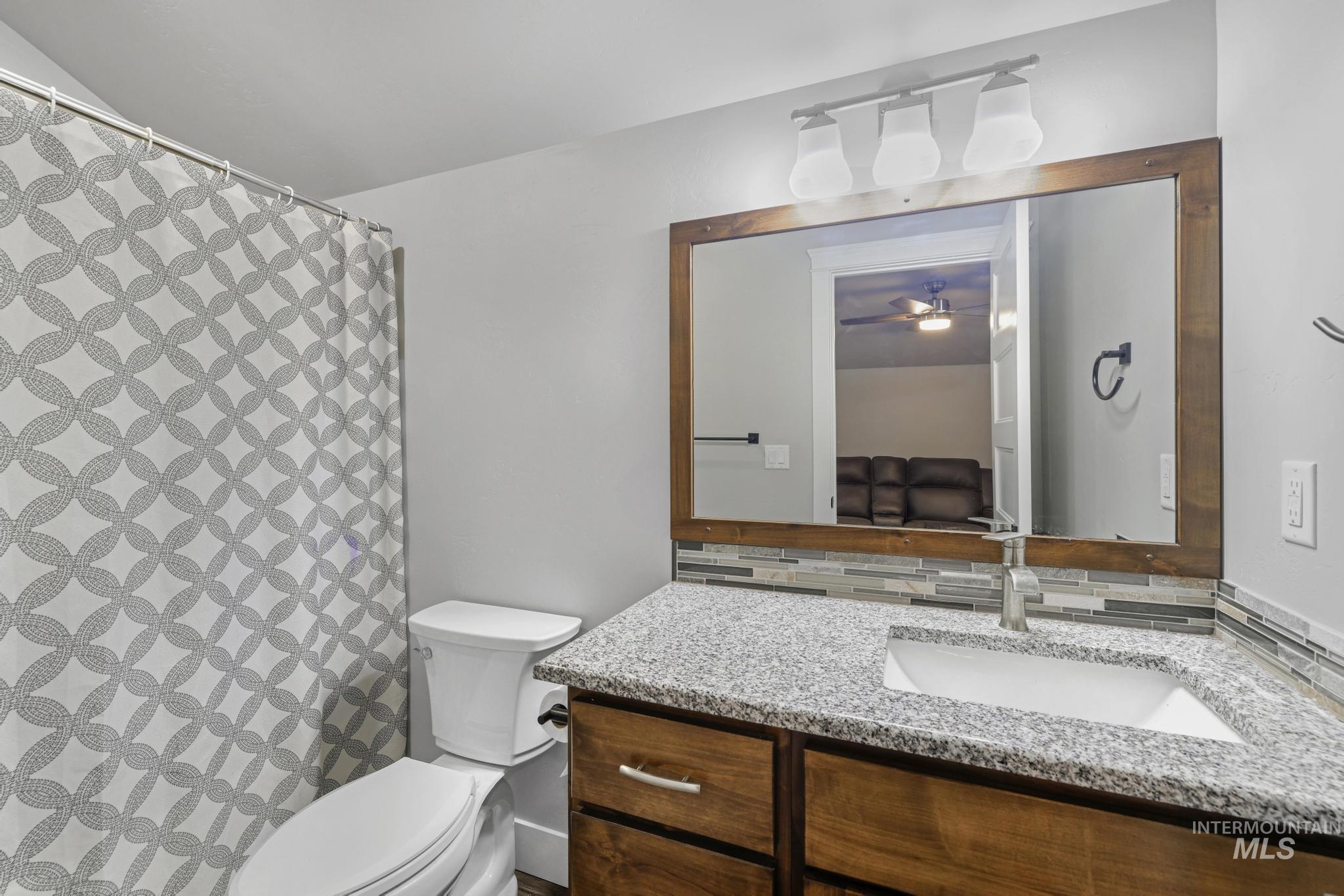 1150 Kimberly Meadows Road Kimberly, ID 83341 - Photo 19 of 32 Bathroom featuring a wood-finish vanity with a granite-style countertop, undermount sink, and a multi-tone tile backsplash