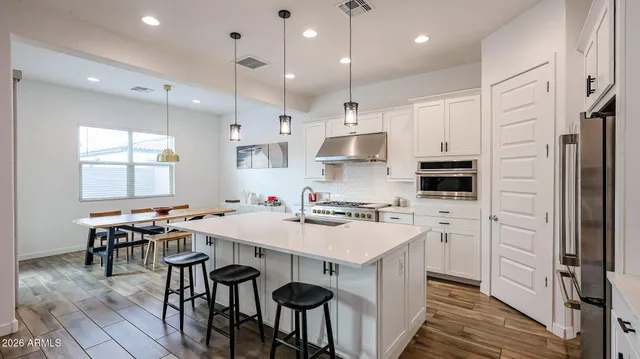 a kitchen with stainless steel appliances a stove a sink a refrigerator white cabinets and chairs