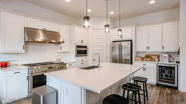 a kitchen with stainless steel appliances a stove a sink dishwasher a refrigerator with white cabinets and wooden floor