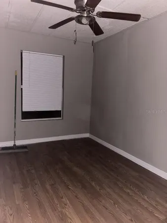 a view of an empty room with wooden floor and a ceiling fan