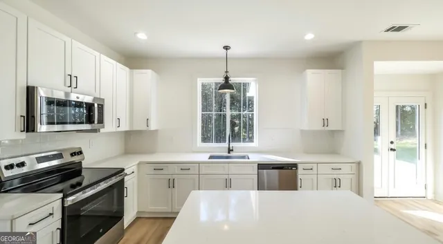a kitchen that has a lot of white cabinets and stainless steel appliances