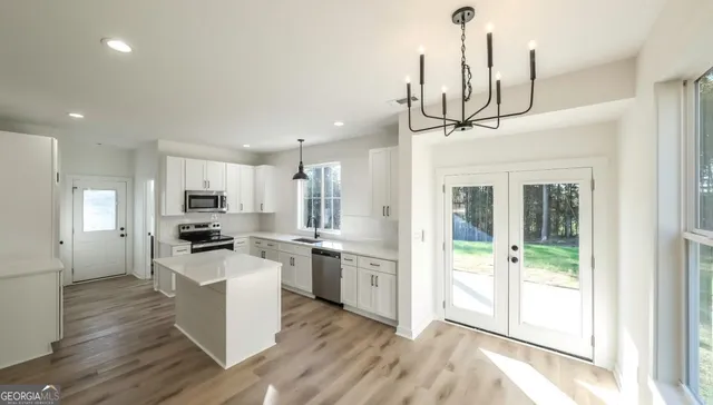 a kitchen with stainless steel appliances kitchen island granite countertop a stove top oven a sink a refrigerator and white cabinets with wooden floor