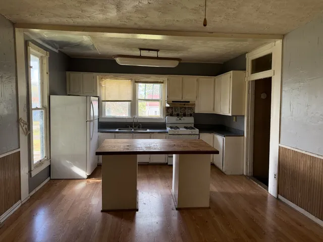 a kitchen with stainless steel appliances granite countertop a refrigerator a sink dishwasher a stove and white countertops with wooden floor