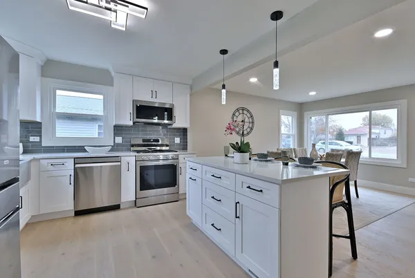 a kitchen with stainless steel appliances granite countertop a stove top oven a sink dishwasher a dining table and chairs with wooden floor