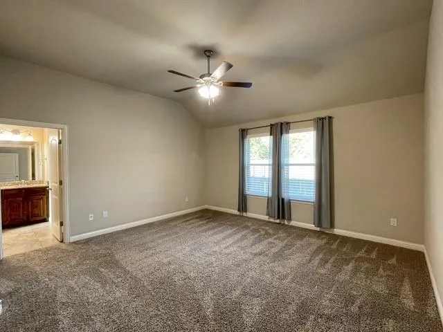a view of an empty room with chandelier fan and windows