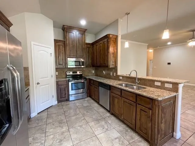 a large kitchen with a large counter top a sink a refrigerator and stainless steel appliances