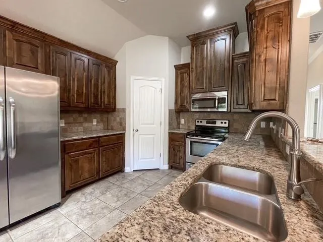 a kitchen with granite countertop wooden cabinets a sink and stainless steel appliances