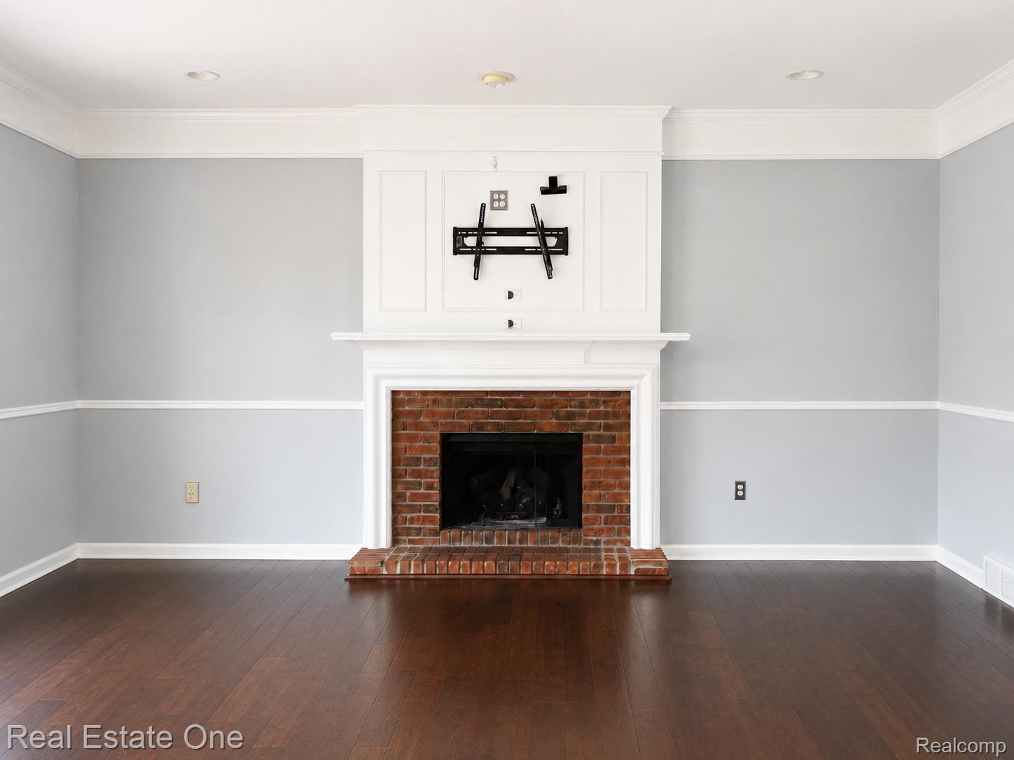 1141 Sandy Ridge Drive Rochester, MI 48306 - Photo 6 of 9 Brick fireplace with a white mantel and paneling, dark wood-finish flooring, two-tone wall paint, crown molding, and recessed lighting