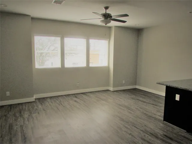 an empty room with wooden floor fan and windows