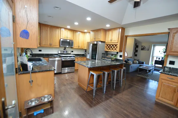 a kitchen with stainless steel appliances granite countertop a refrigerator a stove top oven a dining table and chairs with wooden floor