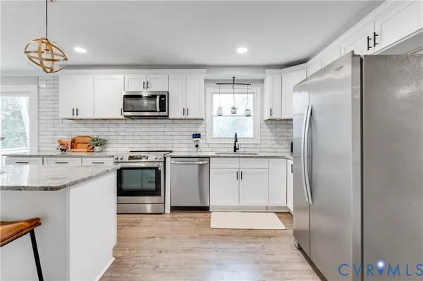 a kitchen with stainless steel appliances granite countertop a refrigerator a stove a sink dishwasher and white cabinets with wooden floor