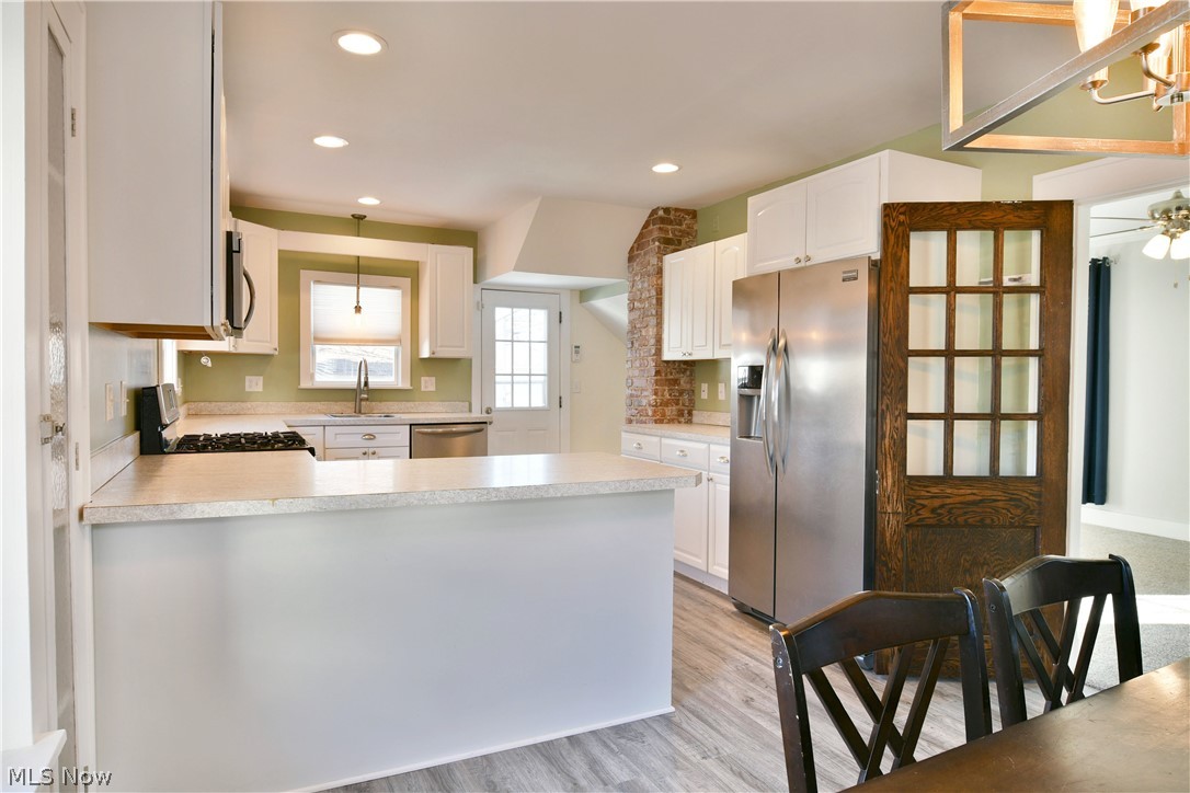 1525 Elm Road Northeast Warren, OH 44483 - Photo 12 of 50 Kitchen with a peninsula, stainless steel appliances, light countertops, white cabinets, and light wood finished floors
