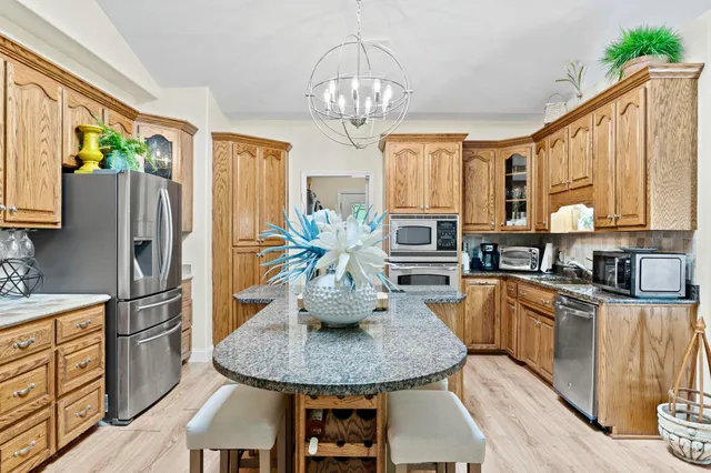 a kitchen with stainless steel appliances granite countertop a refrigerator a sink dishwasher a dining table and chairs with wooden floor