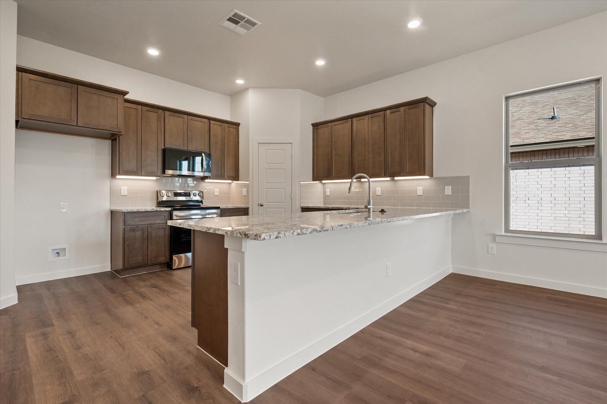7207 7th Street Lubbock, TX 79416 - Photo 5 of 22 a kitchen with stainless steel appliances kitchen island granite countertop a refrigerator and a stove top oven