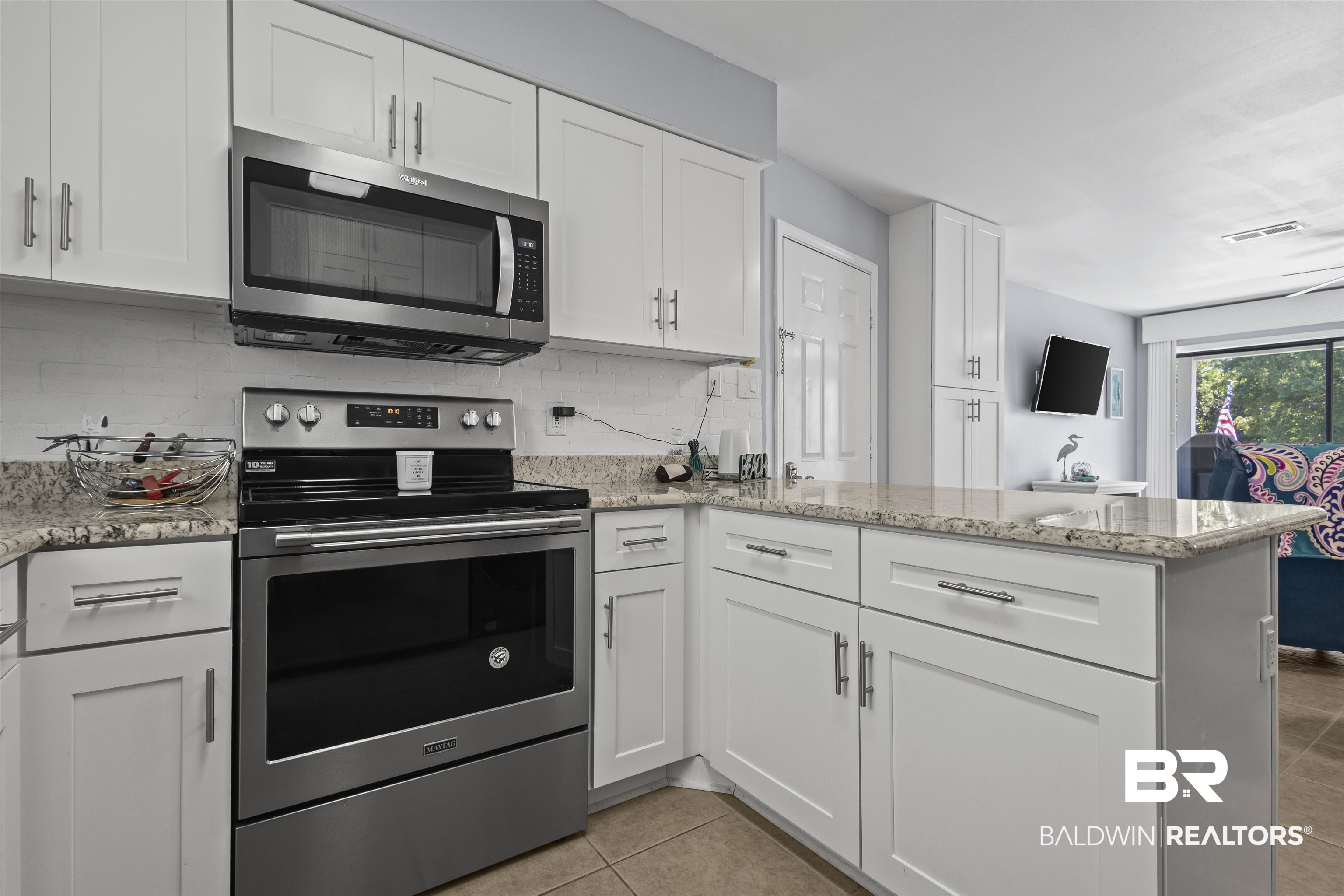 25925 Canal Road, Unit 207 Orange Beach, AL 36561 - Photo 19 of 42 Kitchen with kitchen peninsula, backsplash, white cabinetry, appliances with stainless steel finishes, and light tile floors