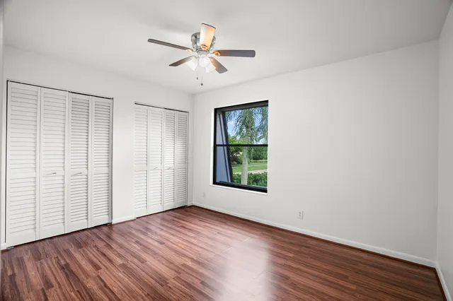 an empty room with wooden floor chandelier fan and windows
