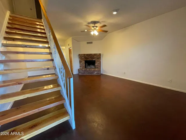 a view of an empty room with wooden floor a ceiling fan and a kitchen view