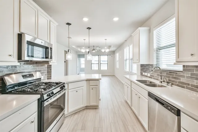 a kitchen with stainless steel appliances a sink dishwasher a refrigerator and a stove top oven with wooden floor