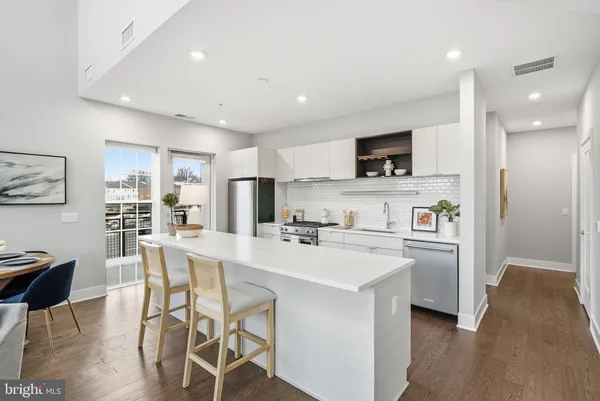 a kitchen with stainless steel appliances a stove a sink a refrigerator and a dining table with wooden floor