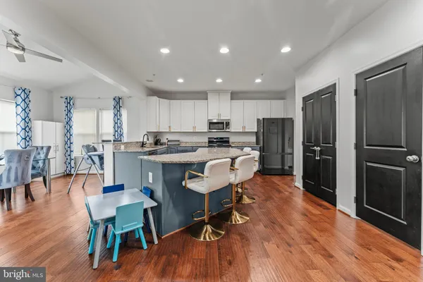 a kitchen with stainless steel appliances granite countertop a refrigerator a stove top oven a sink dishwasher a dining table and chairs with wooden floor