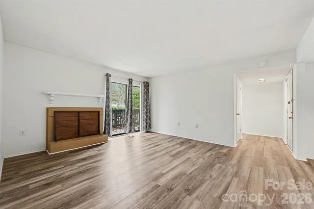 a view of an empty room with wooden floor fireplace and a window