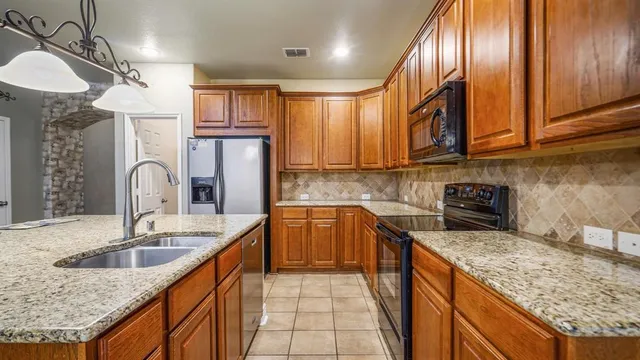 a kitchen with granite countertop stainless steel appliances a sink dishwasher refrigerator stove and cabinets
