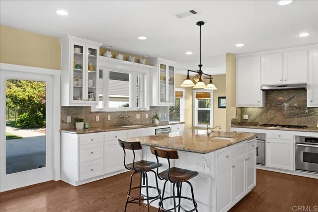 a kitchen with kitchen island granite countertop a stove a sink dishwasher and white cabinets with wooden floor