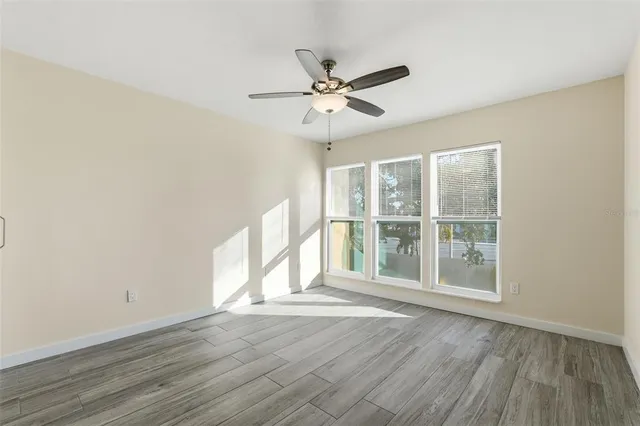 an empty room with wooden floor fan and windows