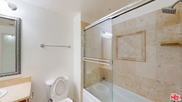 a bathroom with a granite countertop bathtub shower sink mirror and toilet