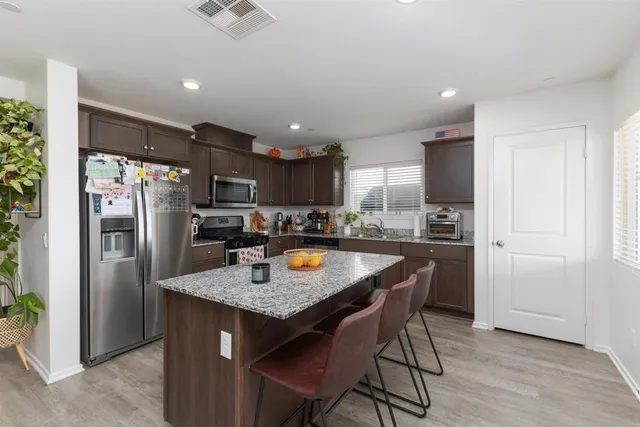 a kitchen with stainless steel appliances granite countertop a refrigerator a sink a stove a dining table and chairs