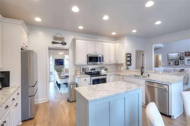 a kitchen with stainless steel appliances kitchen island granite countertop a stove top oven a sink a refrigerator and white cabinets